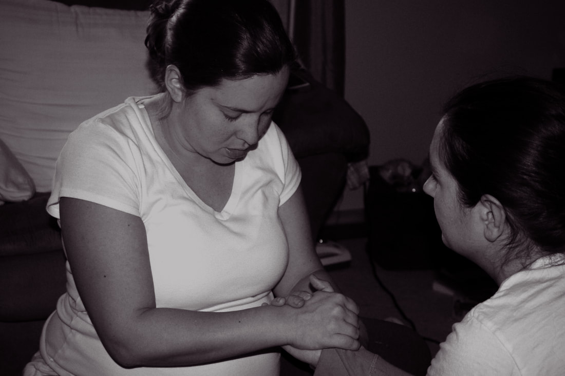 Black and white photo of a pregnant mother squatting during labor with the support of a doula