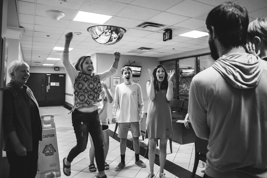 Black and white photo of a family cheering in excitement in a hospital waiting room after the birth of a new baby | Charleston, ,SC birth photography