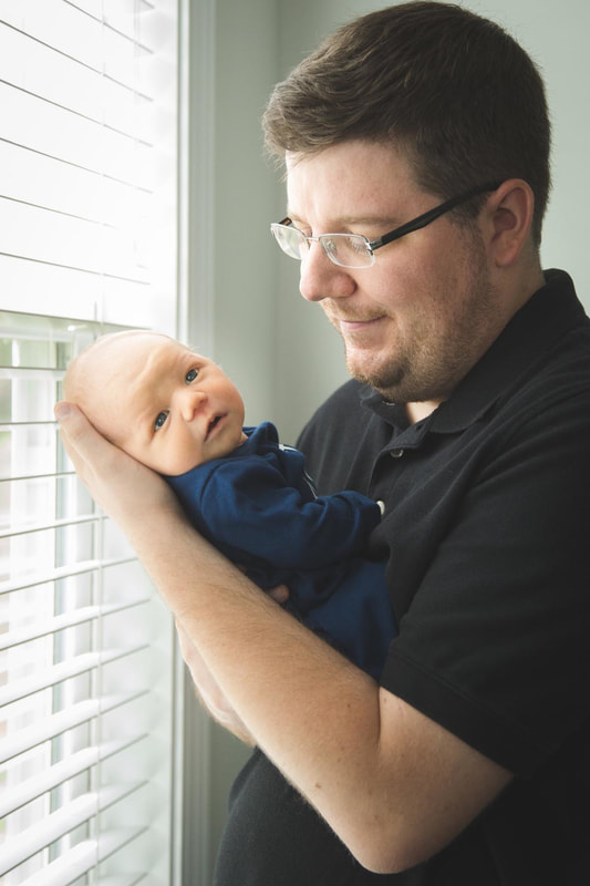 dad holding his newborn son by a window during lifestyle newborn session in charleston sc