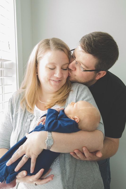 Photo of dad kissing mom on the cheek while she looks down at her newborn son during an in home photography session in charleston sc
