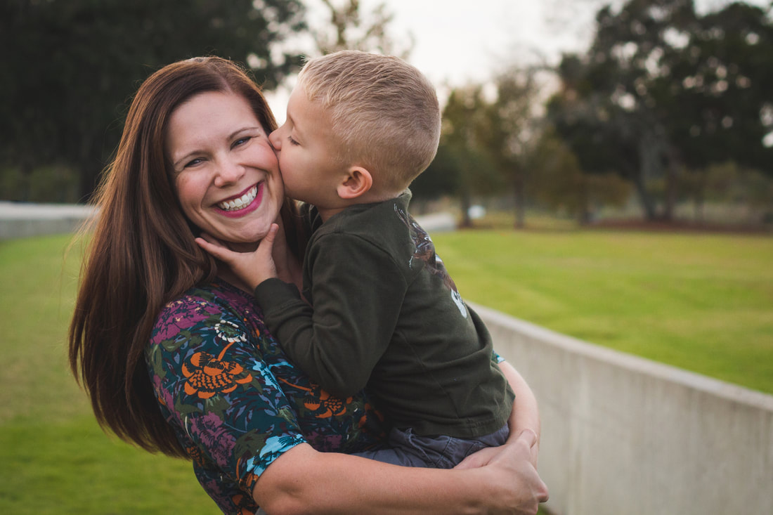 Photo of a mom smiling holding her preschool age son as he kisses her cheek - Family Portrait Session North Charleston, SC